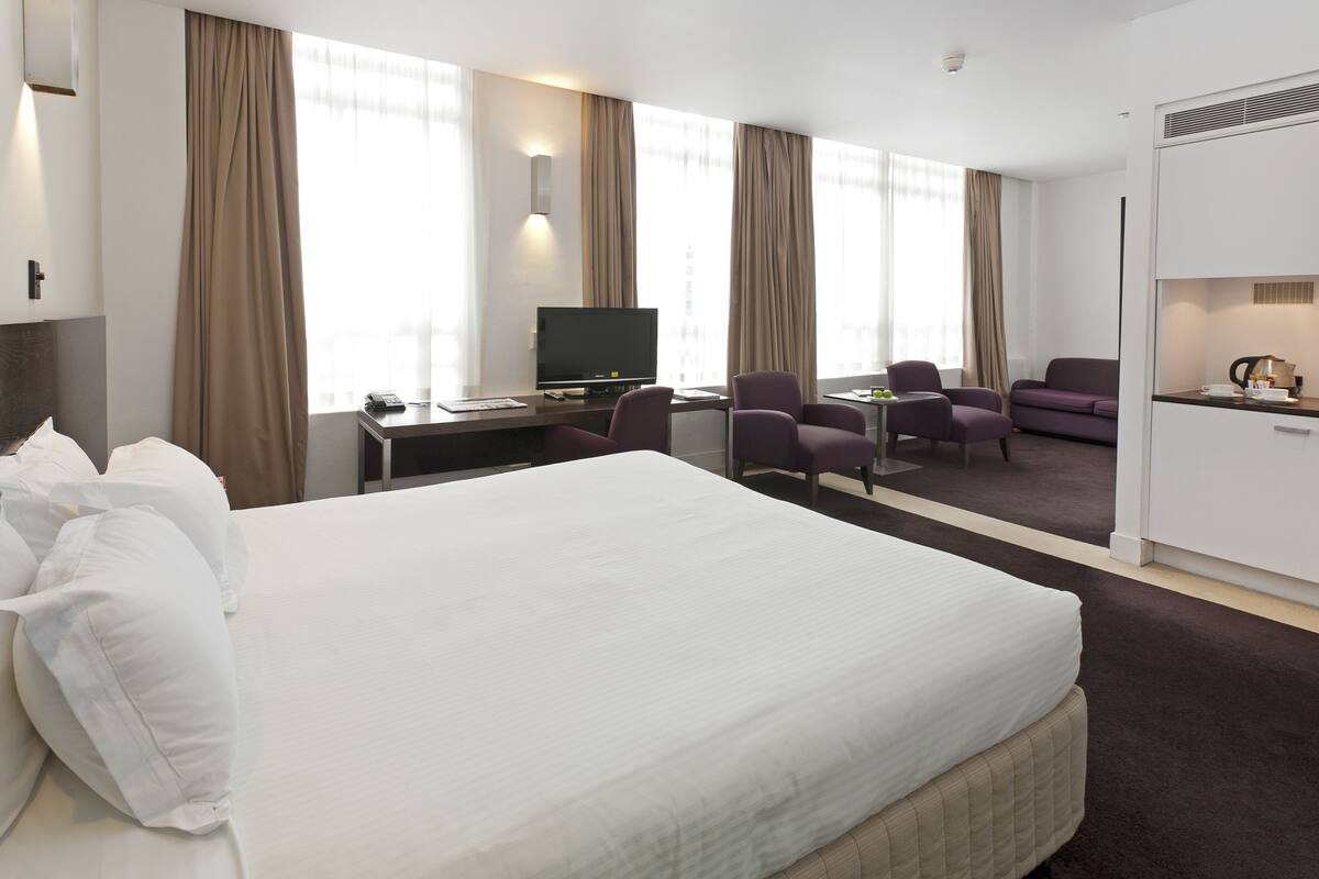 A hotel room with a large bed, a desk with a computer, a TV, and two chairs.