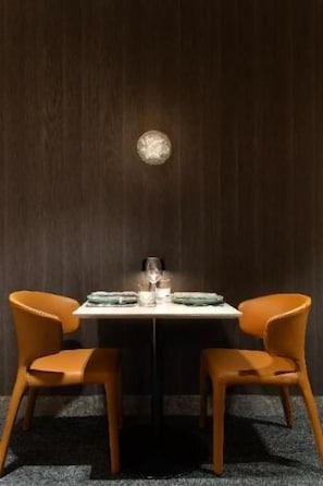 Una mesa de comedor con dos sillas, un vaso y un plato frente a una pared de madera oscura.