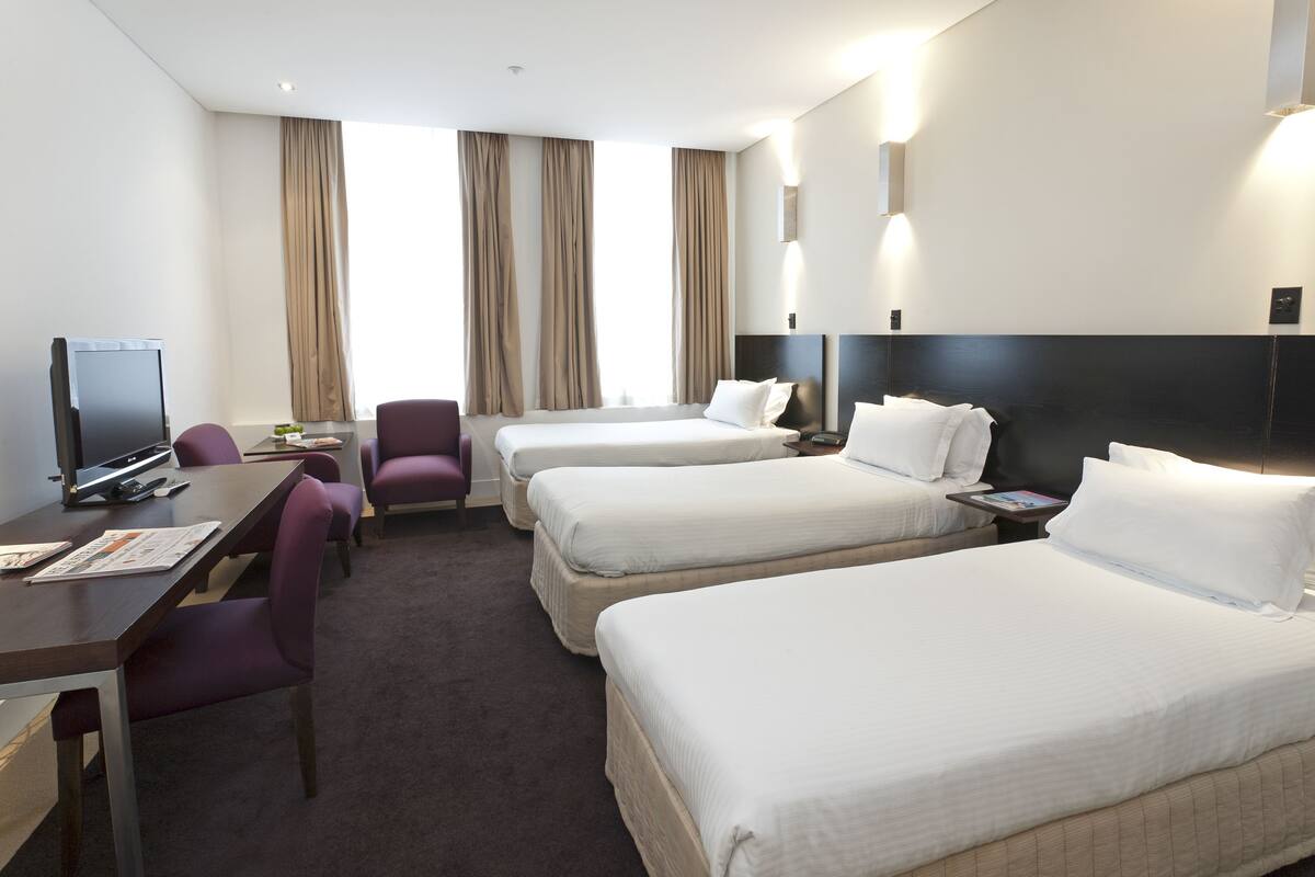 A hotel room with two beds, a desk with a computer, a chair, and a TV.