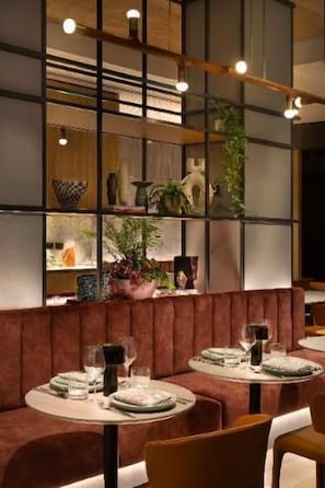 Interior de un restaurante con área de mesas tipo cabina, mesas dispuestas con vajilla y un estante en la pared con objetos decorativos.