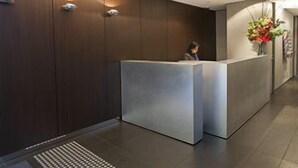 Un comptoir d’accueil dans un hall moderne, avec un panneau indiquant que le sol est glissant, un arrangement floral et une personne debout derrière le comptoir.