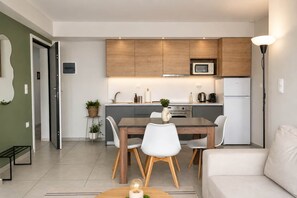 A modern kitchen with wooden cabinets, a microwave, and a refrigerator. There is a dining table with chairs and a small plant on the side. - Bright 1BR Apartment 5 min to Ladadika (Thessaloniki)
