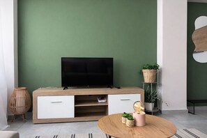A modern living room with a flat-screen TV on a wooden cabinet, a round coffee table with decorative items, and a green accent wall. - Bright 1BR Apartment 5 min to Ladadika (Thessaloniki)