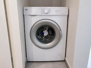 A compact, white front-loading washing machine with a control panel on the top. - Bright 1BR Apartment 5 min to Ladadika (Thessaloniki)