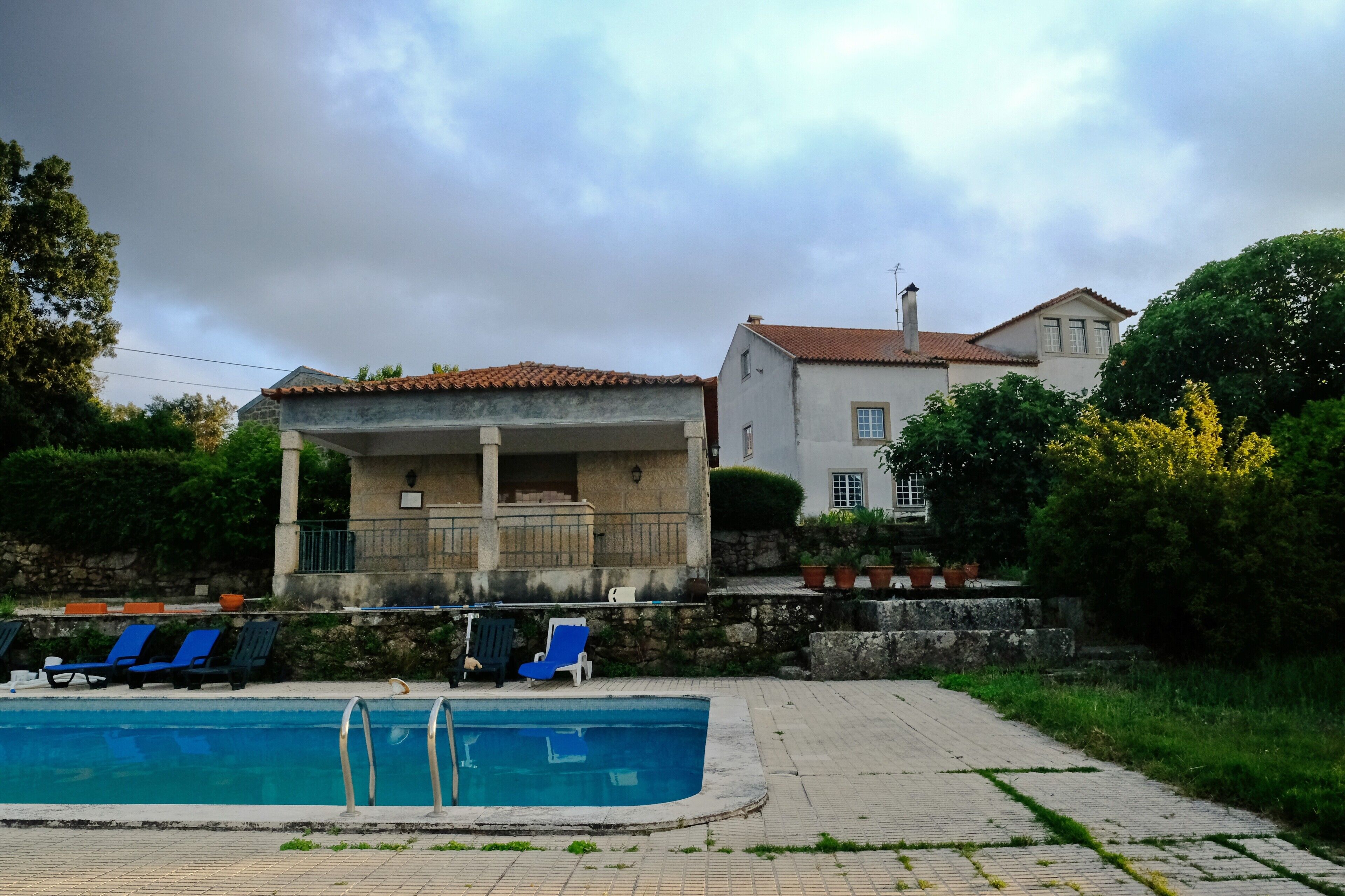 Ein Schwimmbecken mit Liegestühlen, ein Gebäude mit Balkon und eine Steinmauer.