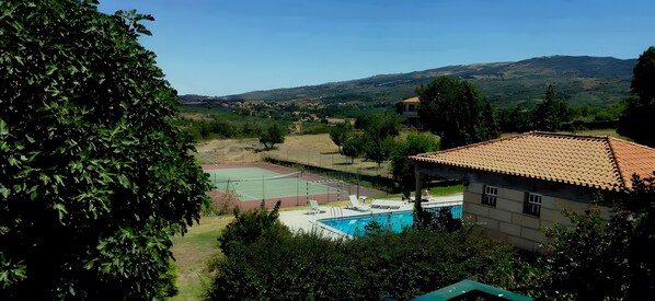 A residential area with a swimming pool, tennis court, and a house with a tiled roof.