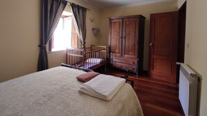 A bedroom with a bed, a wooden wardrobe, a radiator, and a window with curtains.