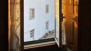 An open doorway leading to a courtyard with a white building, a wooden door, and a window.