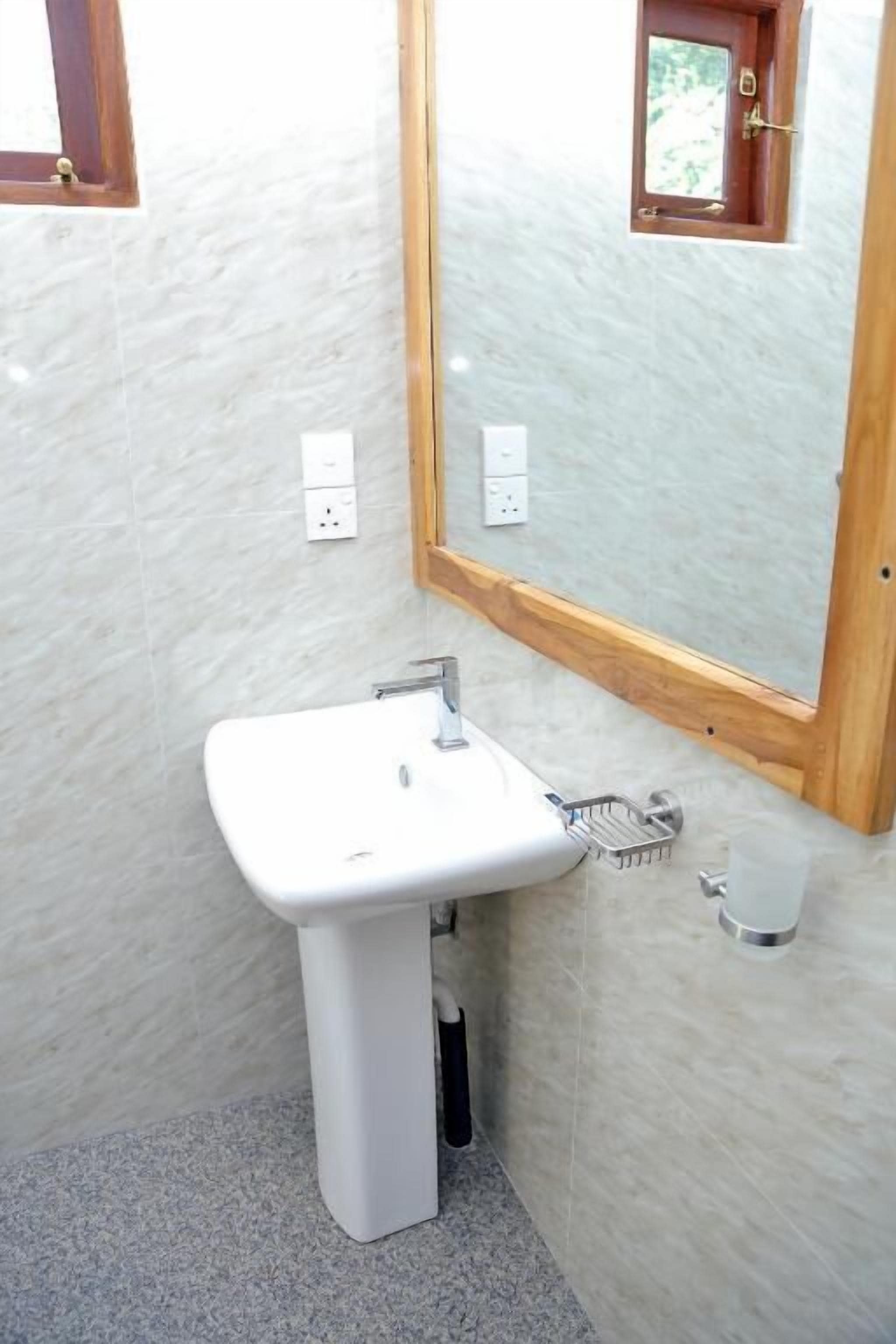 Un baño con un lavamanos blanco, un espejo con marco de madera y una ventana pequeña.