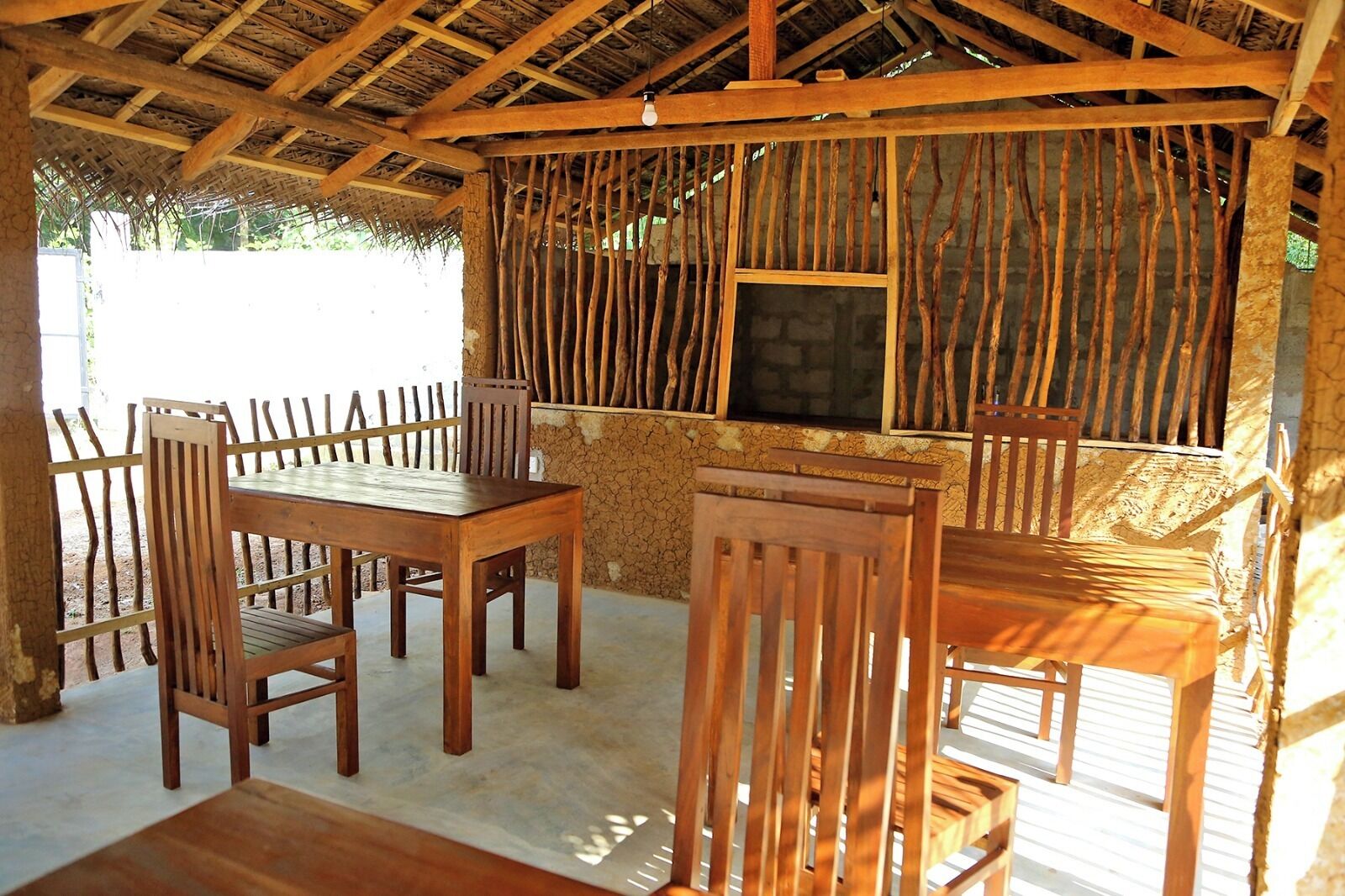 A rustic wooden dining area with a table and chairs, a thatched roof, and a window with a view.