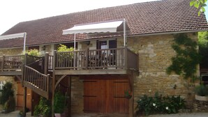 A stone building with a wooden balcony, a staircase, and a covered entrance. - Holiday Home “Gîte Le Séchoir” with Shared Pool, Wi-Fi and Air Conditioning (Le Vignon-en-Quercy)