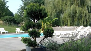 A pool area with white lounge chairs, a small tree, and a concrete planter with lavender plants. - Holiday Home “Gîte Le Séchoir” with Shared Pool, Wi-Fi and Air Conditioning (Le Vignon-en-Quercy)