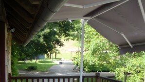 A wooden deck with a table and chairs, surrounded by greenery and a view of a grassy area. - Holiday Home “Gîte Le Séchoir” with Shared Pool, Wi-Fi and Air Conditioning (Le Vignon-en-Quercy)
