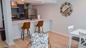 A modern kitchen with a central island, bar stools, a dining table, and a decorative wall piece. - Waterfront Coastal Escape (Atlantic Beach)