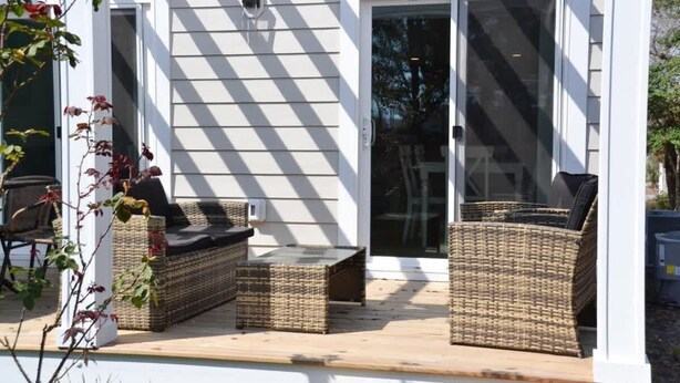 A covered outdoor seating area with wicker furniture and a sliding glass door. - Waterfront Coastal Escape (Atlantic Beach)