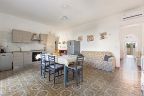 A kitchen with a dining table, chairs, and a sofa. There is a refrigerator, a microwave, and a sink. The floor has patterned tiles. - Casa Mare Blu by BarbarHouse (San Pietro in Bevagna)