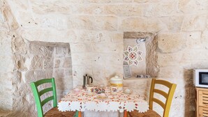 A stone-walled room with a table covered by a lace tablecloth, two chairs, a kettle, and a television. - Beltrullo Pietrevive by BarbarHouse (Martina Franca)