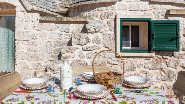 A stone building with a table set for dining, a basket, and a window with green shutters. - Beltrullo Pietrevive by BarbarHouse (Martina Franca)