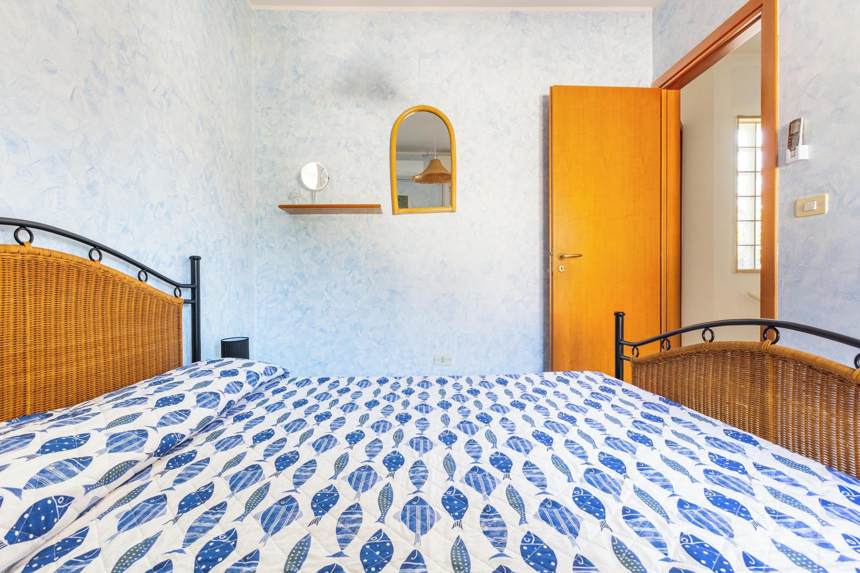 A room with two wicker beds, a mirror, a shelf, and a door.