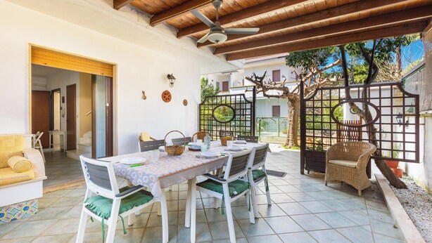 Un patio techado con una mesa de comedor, sillas y un sillón de mimbre.