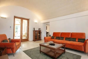 Una sala de estar con un sofá, un sillón, un aparador de madera y una mesa de centro de vidrio.