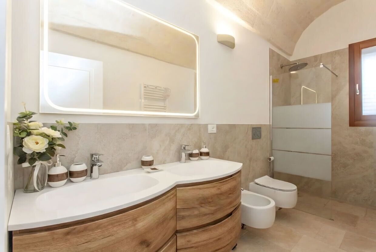 A modern bathroom with a curved vanity, a large mirror, a shower enclosure, and a toilet.