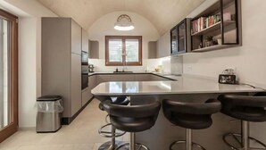 Et moderne køkken med en central ø, barstole, en bogreol og en skraldespand.