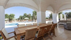 En udendørs terrasse med et træbord og stole, en pool og liggestole.
