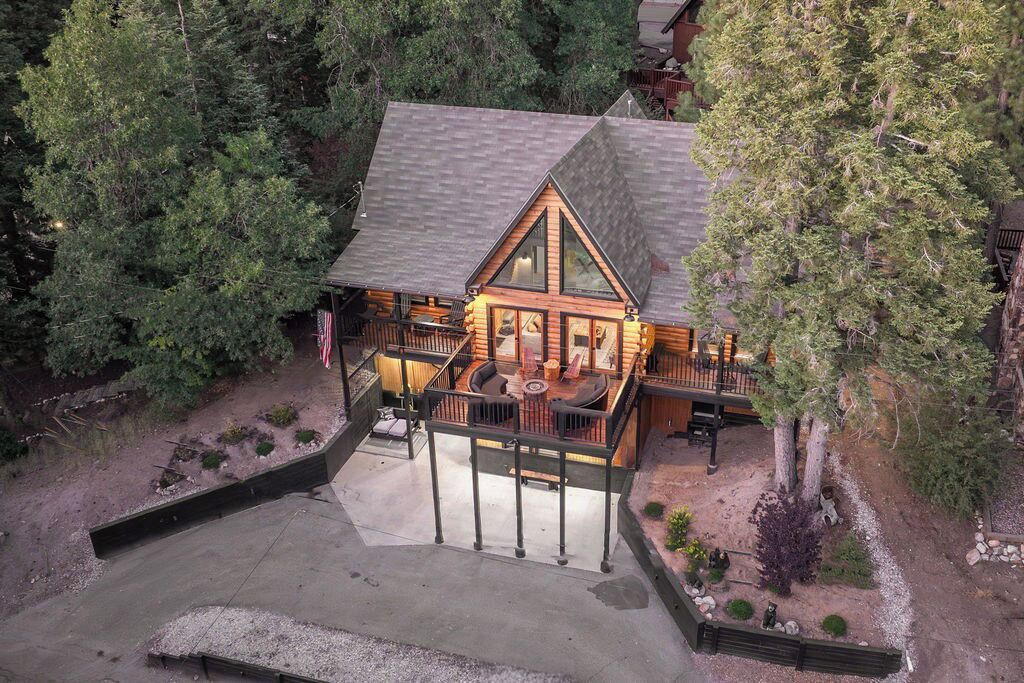 A log cabin with a large deck, surrounded by dense forest.