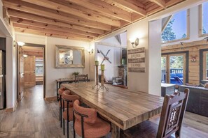Un vaste espace dédié à la salle à manger, avec une longue table en bois, plusieurs chaises et un plafond au style rustique.