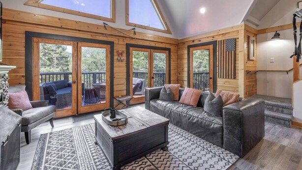 Ein gemütliches Interieur mit Holzbalkendecke, großen Fenstern, einem Ledersofa und einem Couchtisch.