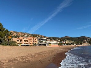 A beachside hotel with multiple buildings, a sandy beach, and a mountain in the background. - Appartement 3 pièces dans résidence de standing avec piscine (Saint-Raphaël)
