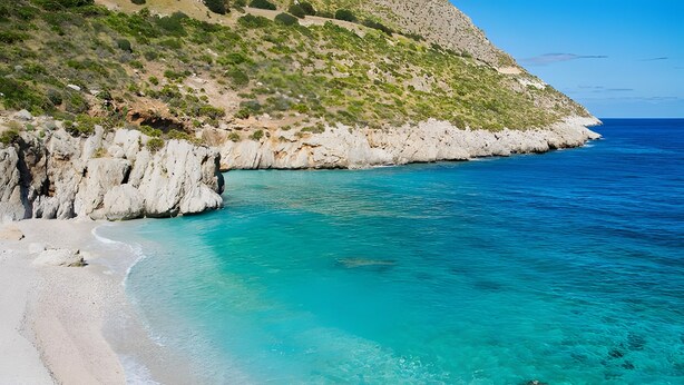 Un paisaje costero con aguas turquesas cristalinas, una playa de arena y acantilados rocosos.