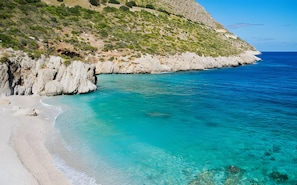A coastal landscape with clear turquoise waters, a sandy beach, and rocky cliffs.