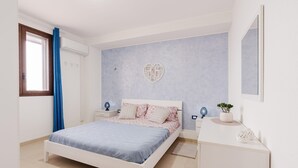 Un dormitorio con cama, mesitas de noche, cómoda, espejo, ventana con cortinas y una decoración en la pared.