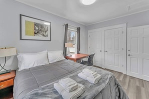 Ein Hotelzimmer mit Bett, Schreibtisch, Stuhl, Lampe, einem gerahmten Bild und einem Kleiderschrank.
