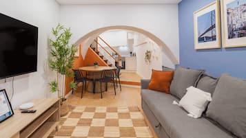Een woonkamer met een flatscreen televisie, een bank, een eettafel met stoelen, een trap en een keuken op de achtergrond.