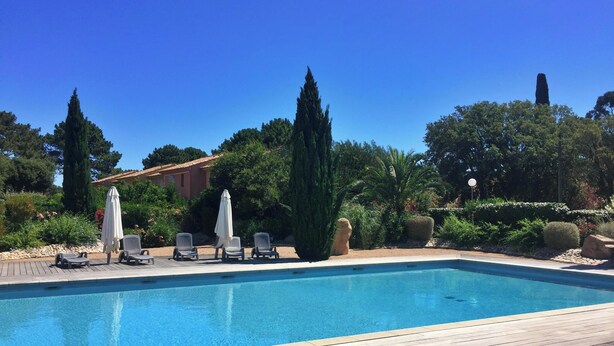 Una piscina rettangolare con un pontile in legno, immersa nel verde e con alcuni lettini e ombrelloni.