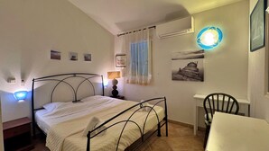 Camera da letto con un letto, una lampada da comodino, condizionatore d'aria a muro e un tavolino con una sedia.