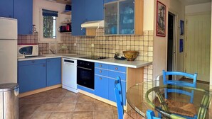 Una cucina compatta con mobili blu, lavastoviglie, forno a microonde e un tavolo da pranzo in vetro con sedie blu.