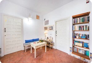 A room with a sofa, a table, a lamp, a bookshelf, and two doors. - Portón 1 Studio – Renovated with Sea Views (Conil de la Frontera)