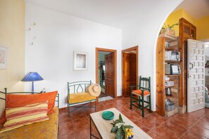 A room with a bed, a table with a bowl and fruit, a chair, a lamp, and a door leading to another room. - Portón 1 Studio – Renovated with Sea Views (Conil de la Frontera)