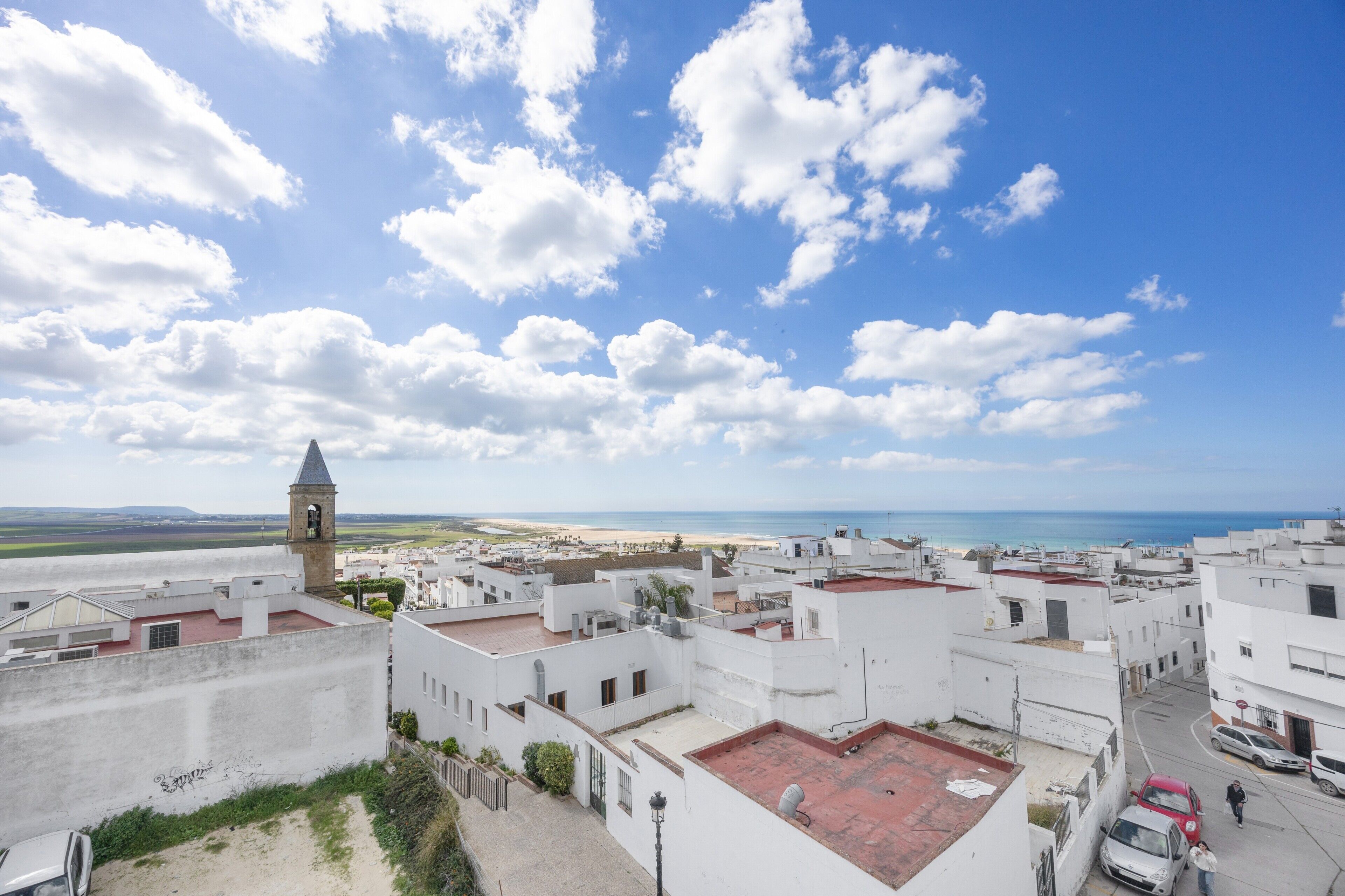 A coastal town with white buildings, a prominent tower, and a beach in the distance.