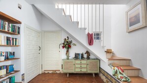 A staircase with a white door, a green cabinet with books, and a tiled floor. - Portón 1 Studio – Renovated with Sea Views (Conil de la Frontera)