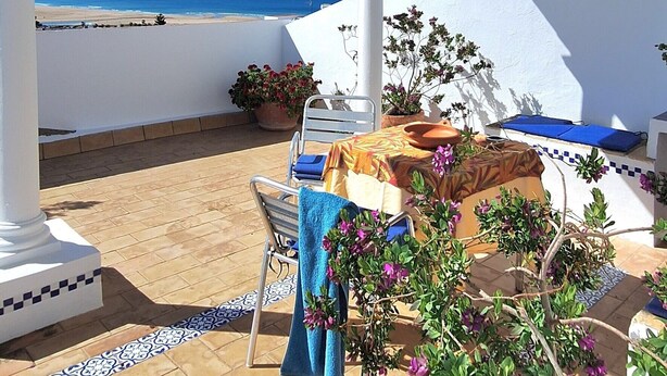 A covered outdoor area with a view of the sea, a table with a chair, and potted plants. - Portón 1 Studio – Renovated with Sea Views (Conil de la Frontera)