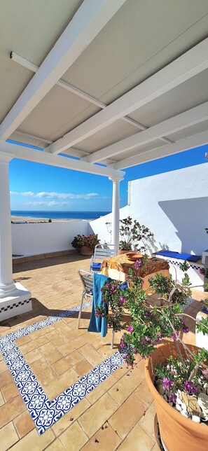 A covered outdoor area with a view of the sea, a table with a chair, and potted plants. - Portón 1 Studio – Renovated with Sea Views (Conil de la Frontera)