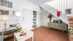 A spacious living area with a staircase, a glass table with books, a lamp, and a bookshelf. - Portón 1 Studio – Renovated with Sea Views (Conil de la Frontera)