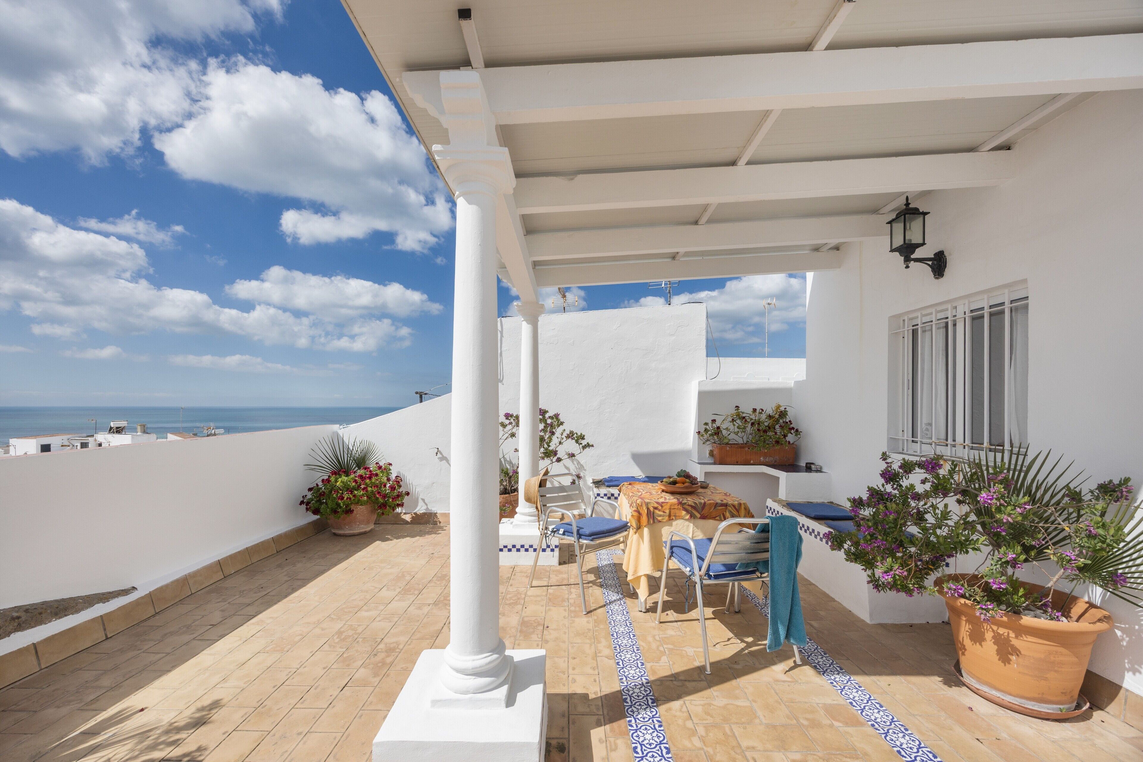 A terrace with a table and chairs, potted plants, and a view of the sea.