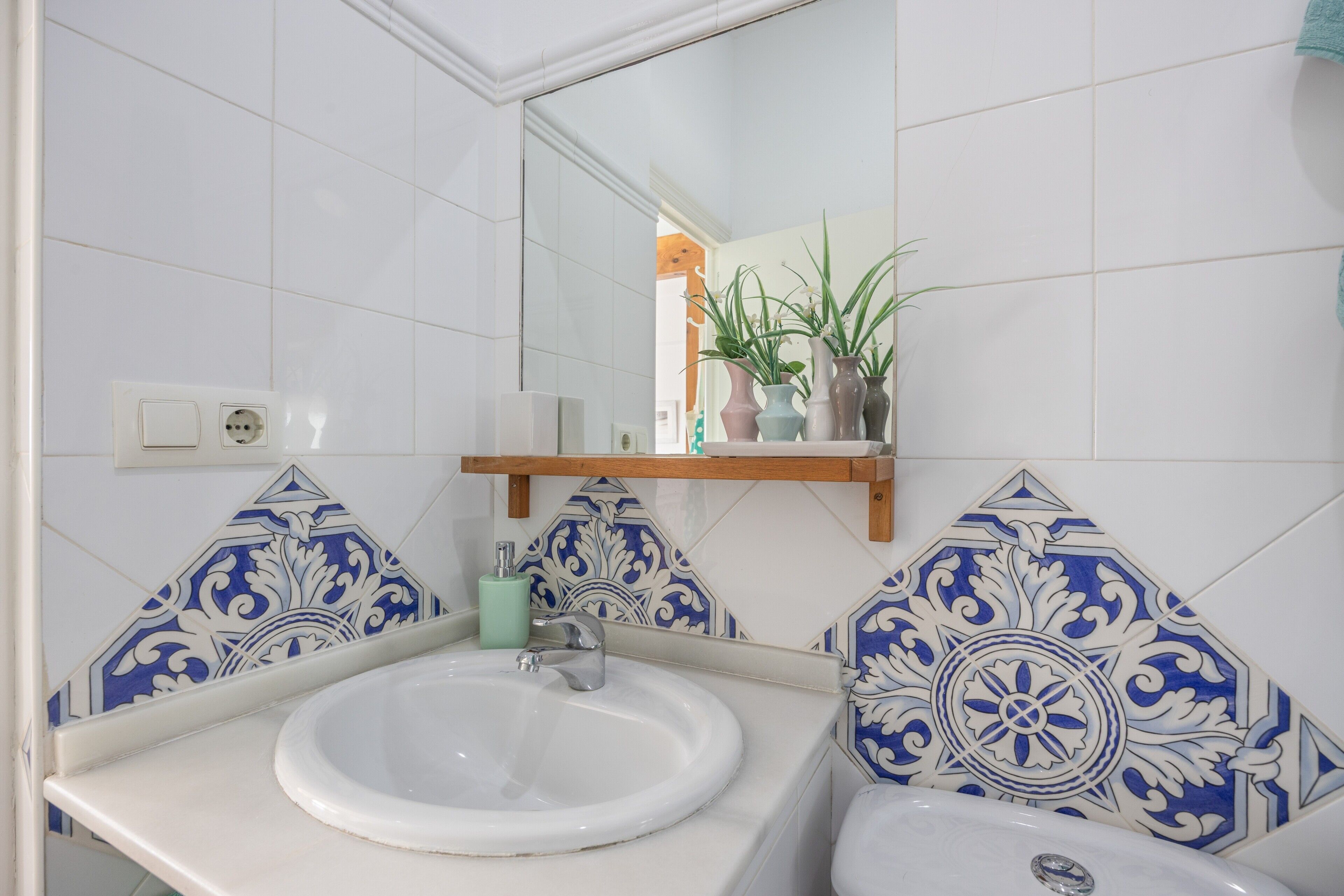Un baño con un lavamanos blanco, un espejo y azulejos azules con diseño.