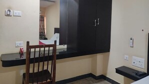 Una habitación con un armario negro, una silla de madera, una mesita y un espejo.